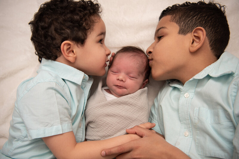 Two brothers kissing their baby brother's forehead.