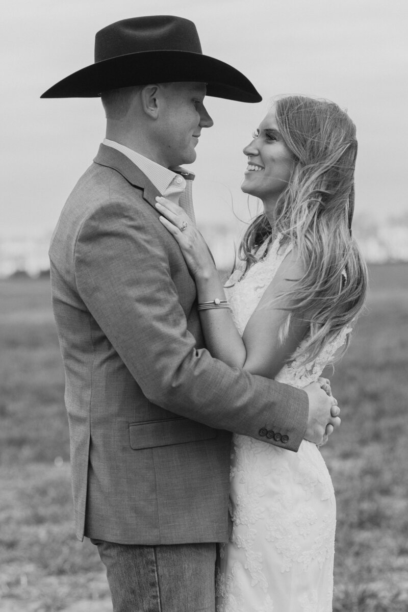 Black and white photo of bride and groom embracing. Groom is wearing a cowboy hat.