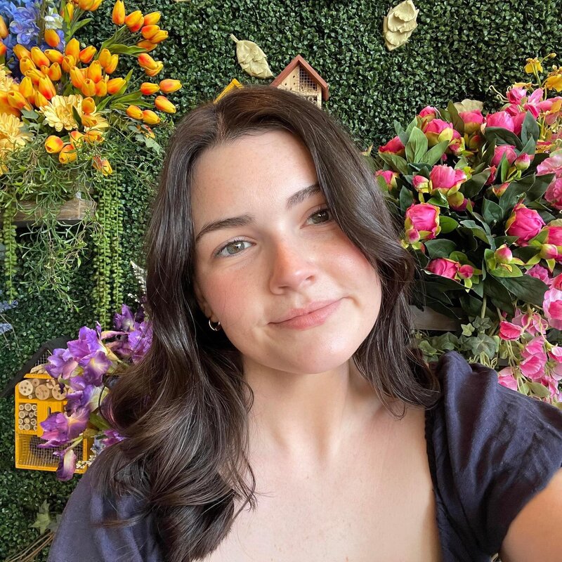 Mackenzie smiling in front of a wall of flowers