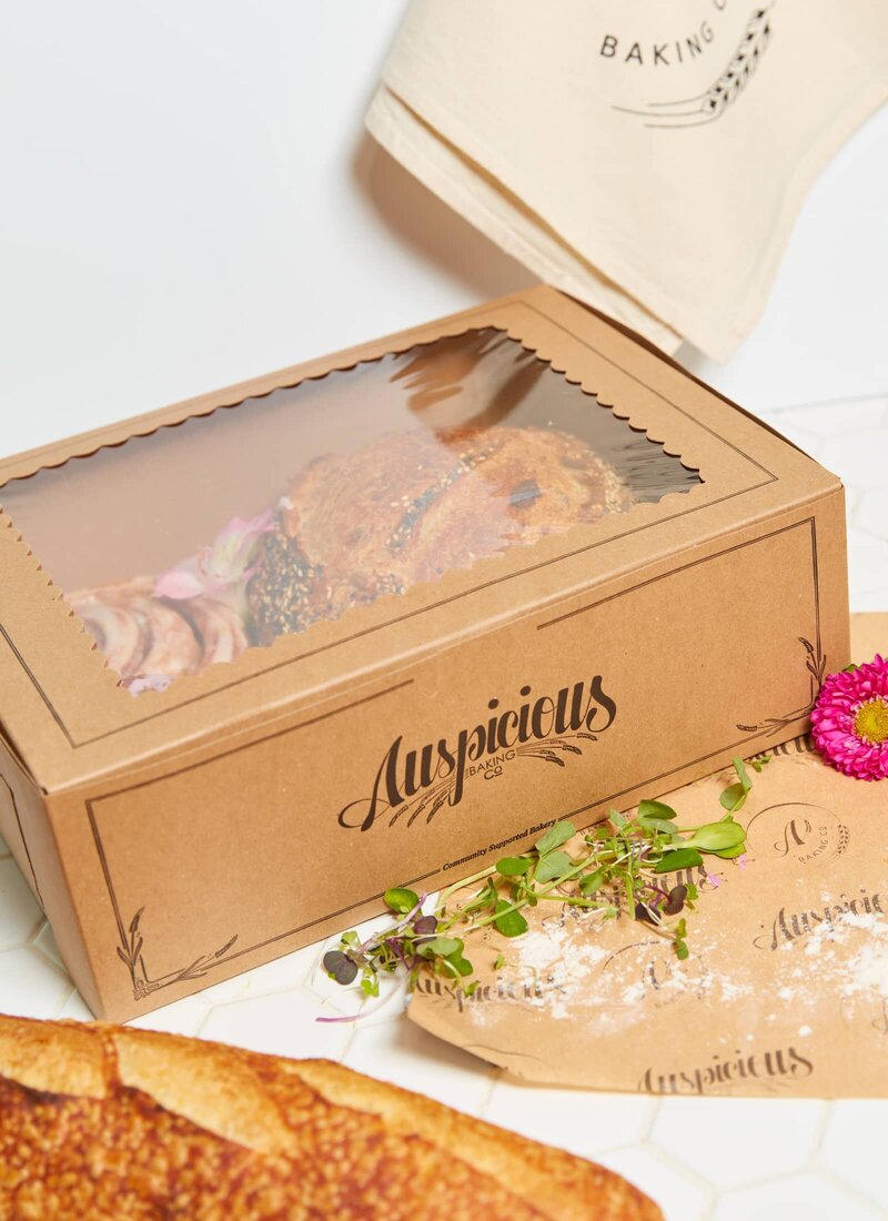 A custom printed, brown kraft bakery box filled with pastries that are visible through the window on top of the box