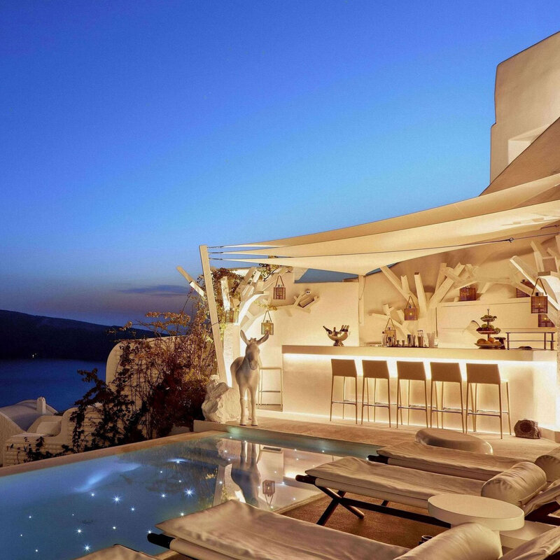 Elegant outdoor bar and pool area illuminated at dusk overlooking the sea.