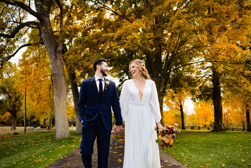 Wedding couple walking towards the camera looking at each other with yellow trees in the background during their fall wedding at Cornman farms in Michigan