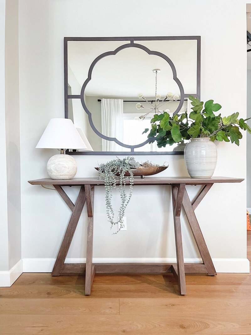 Entryway styled with a wooden table, plant, large mirror and a lamp.