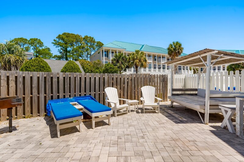 Private fenced-in patio with loungers, Adirondack chairs, BBQ grill, and shaded daybed—ideal for sunny beachside relaxation.