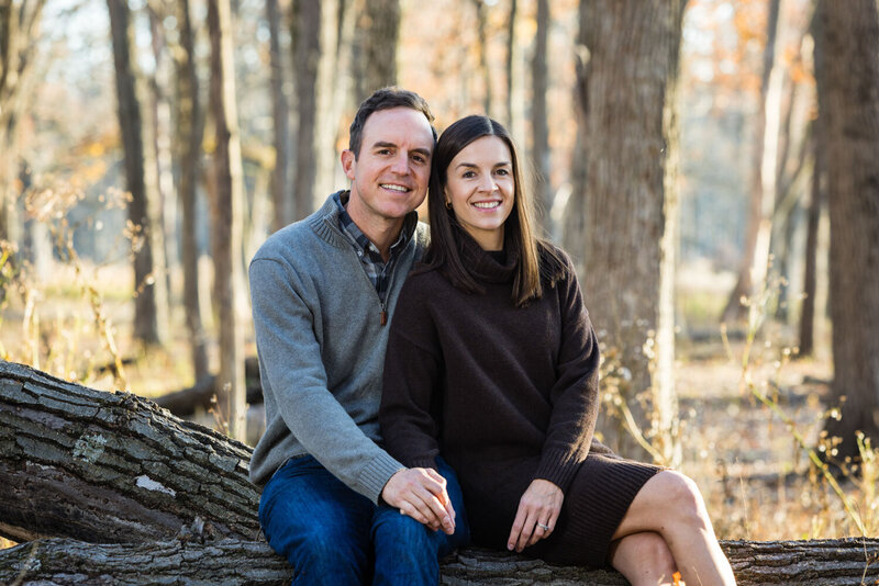 Couple sitting on a fallen tree trunk in a forest, smiling at the camera