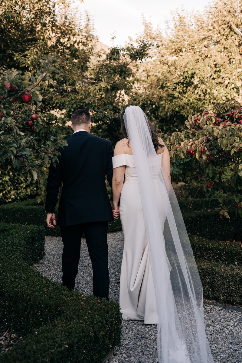 a newly married couple walk through an orchard at their queenstown wedding