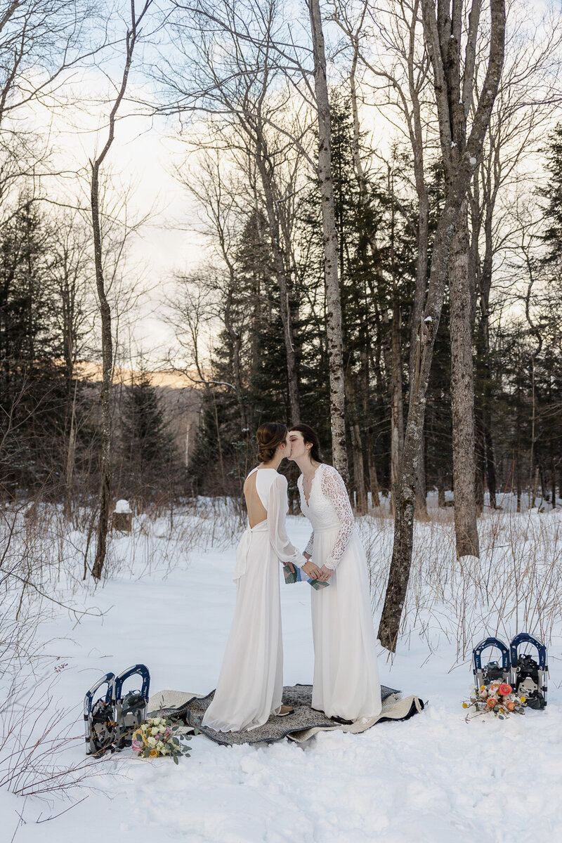 A couple leans in for a kiss surrounded by snow.