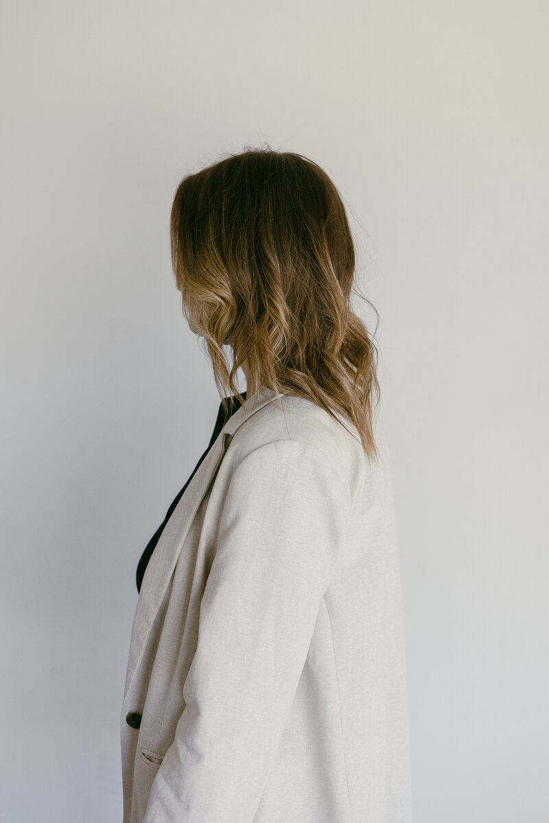 the profile of Caitlin, the photographer, wearing a beige blazer and a black shirt. 