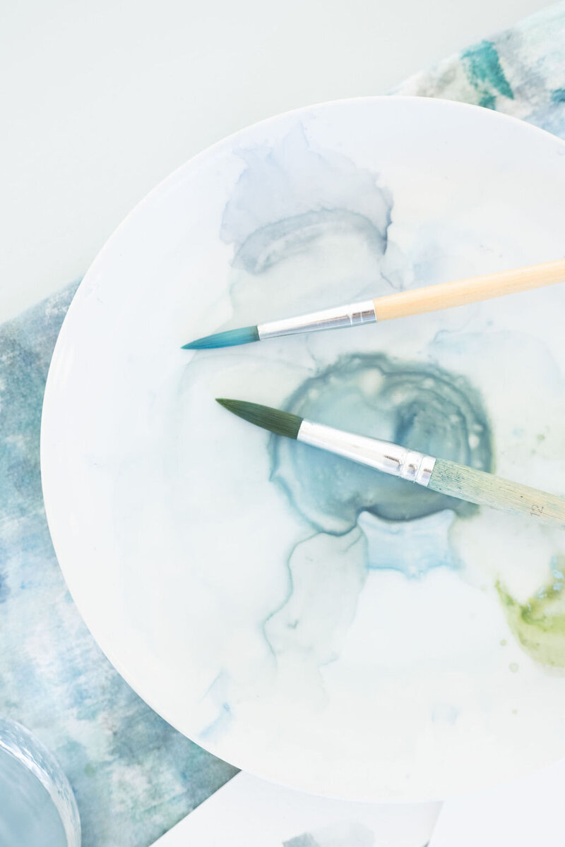 two paintbrushes dipped in blue paint resting over a white palette