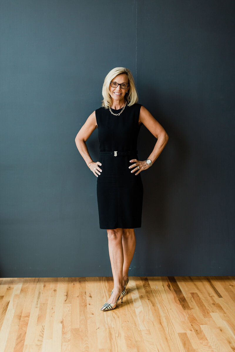 personal branding image of woman standing and smiling black backdrop black dress