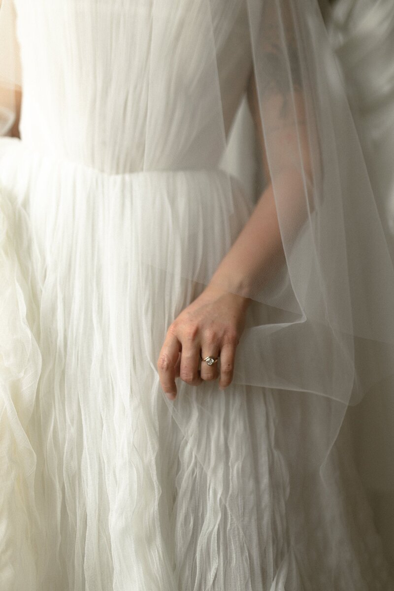 Close-up of a bride’s hand with a ring, holding the skirt of her gown.