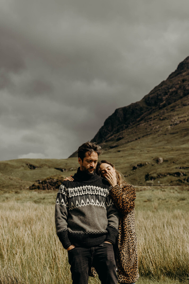Scotland couple portrait with two people wearing sweaters and embracing with the green hills behind them