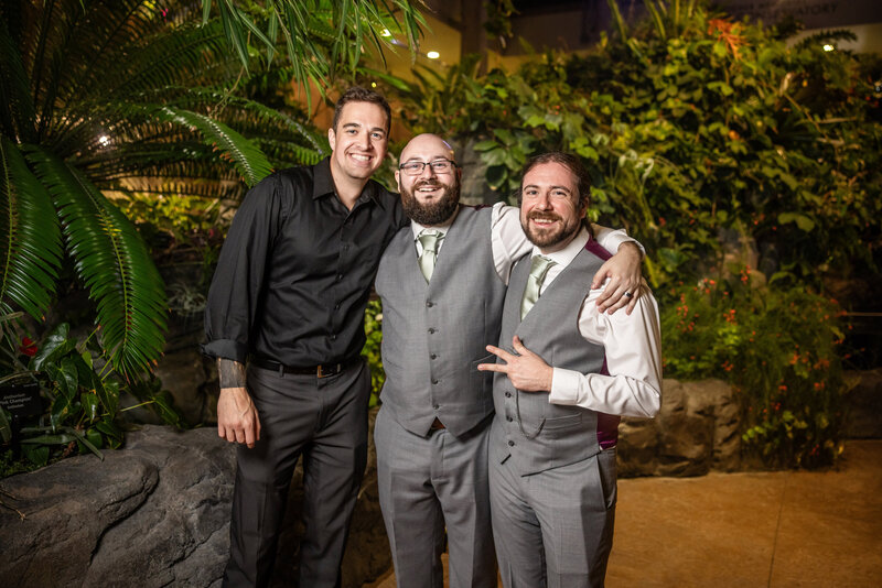 Candid photo of friends in front of a plant backdrop at Marnie's Pavilon Wedding Reception