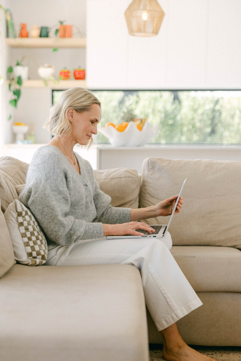 Zelda Green, photographer, financial educator, podcaster and business mentor, sitting on a couch while working on her laptop