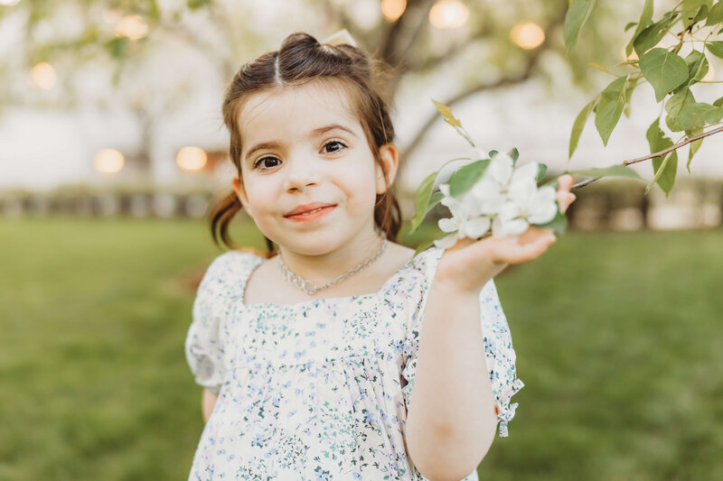 little brown haired girl holding a flower and smiling