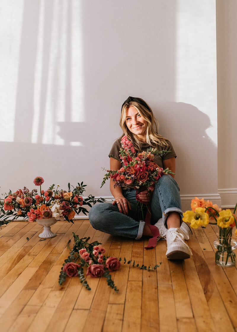 Florist sitting on the ground surrounded by floral arrangements