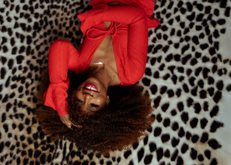 close up boudoir portrait of black woman in red lingerie laughing on animal rug elkridge