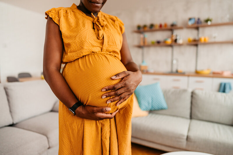 woman in yellow, holding pregnant belly