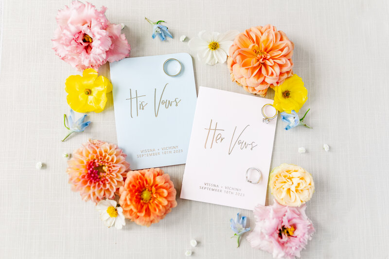 wedding vow cards surrounded by wedding rings and colorful flowers