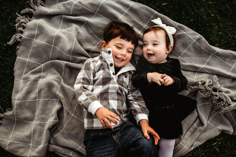 Family photographers Maryland captures little boy laying on a blanket outside with his baby sister for their fall family photos