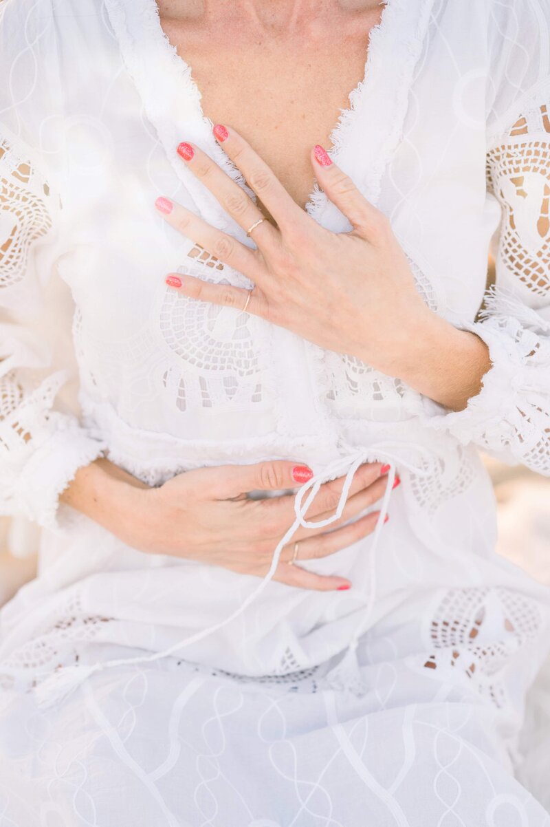 Woman in a white dress with one hand on her heart and the other on her solar plexus, sitting in a peaceful meditative state.