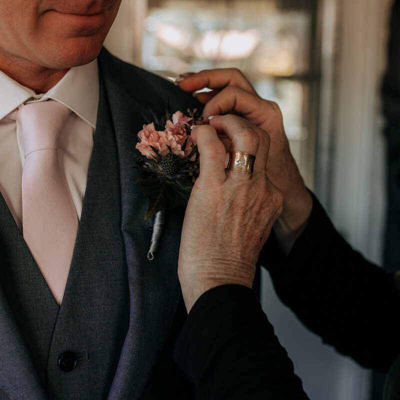 mother of the bride pinning boutonnière on her son
