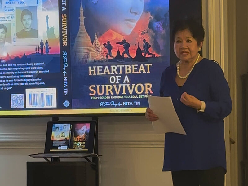 Nita Tin interviewed on Channel 9 Chattanooga’s This and That series. She is seated in a studio blue chair next to host James Howard, who holds her book Heartbeat of a Survivor. A small table with a plant sits between them, with a backdrop screen displaying her name and book graphic.