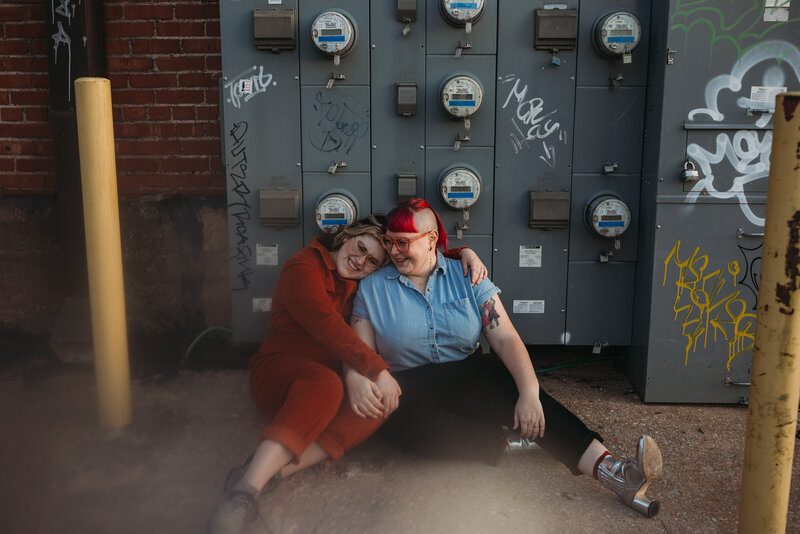 A couple smiling and sitting in front of an electrical box.