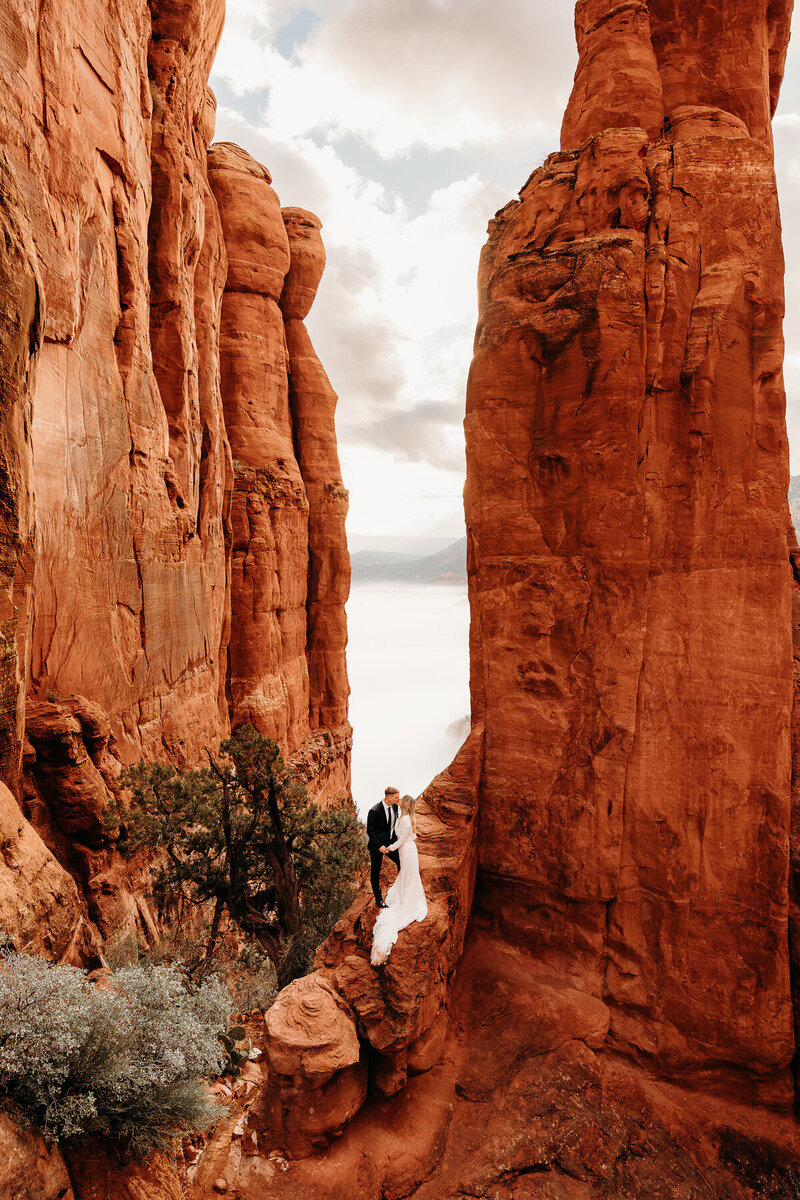 bride and groom embracing on a rock in front of a red rock spire at Cathedral Rock in Sedona AZ for their elopement