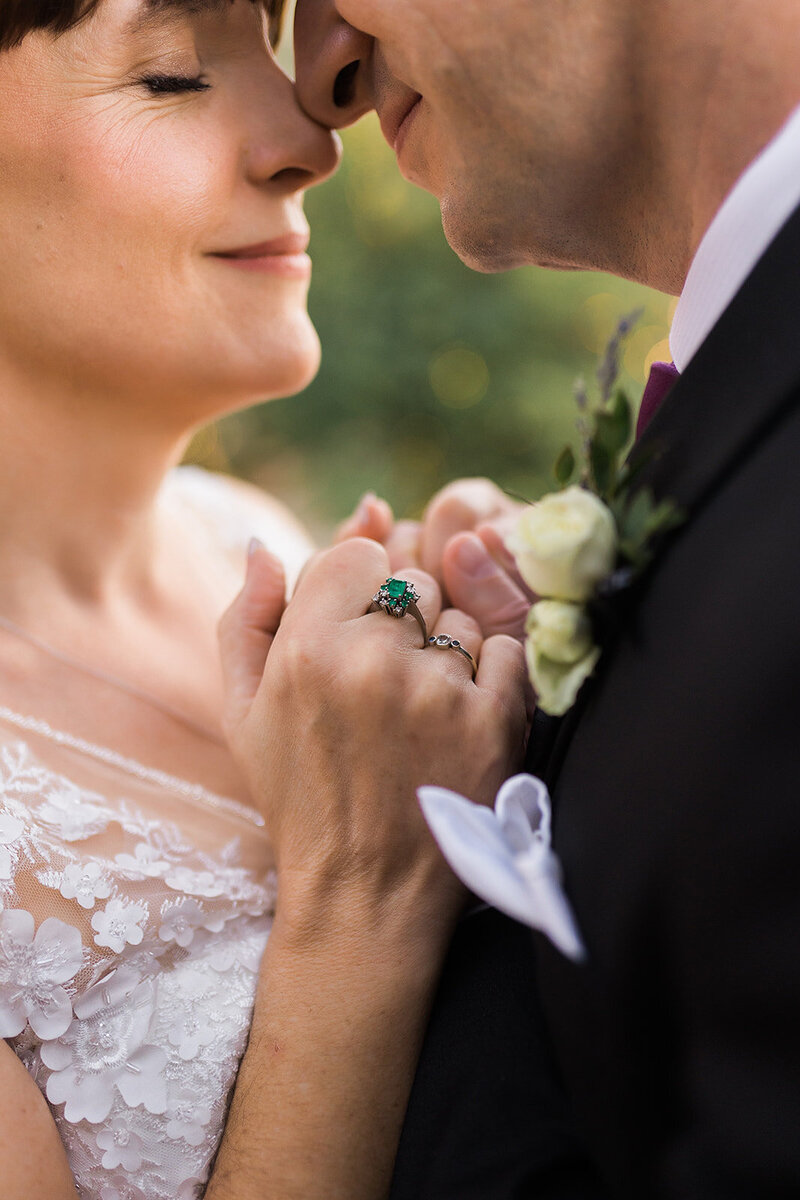 Close up of bride and groom nuzzled, focused on a green ring