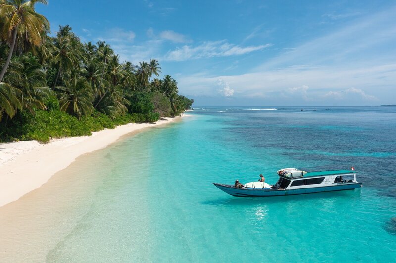 Boat docking on island on a beautiful beach in remote Indonesia - Santai Retreats Longboarding Retreat