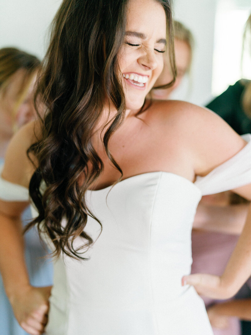 Bride laughing while zipping up her dress