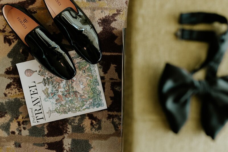 A pair of black shoes and a bow tie on a rug.