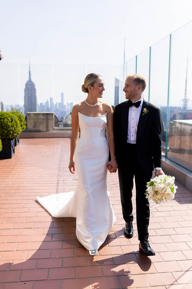 Bride and groom holding hands on the roof at the Rainbow Room with the Empire State Building in the background