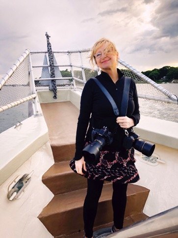 Smiling portrait of photographer Karen Lewis in action on a boat on Casco Bay with 2 cameras