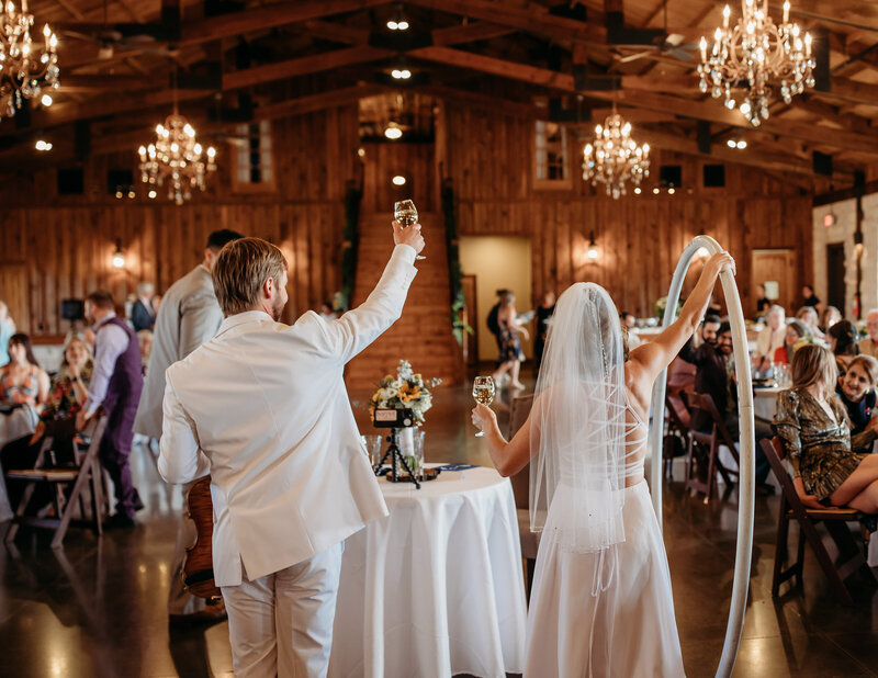 A newlywed couple raising their glasses during their reception.