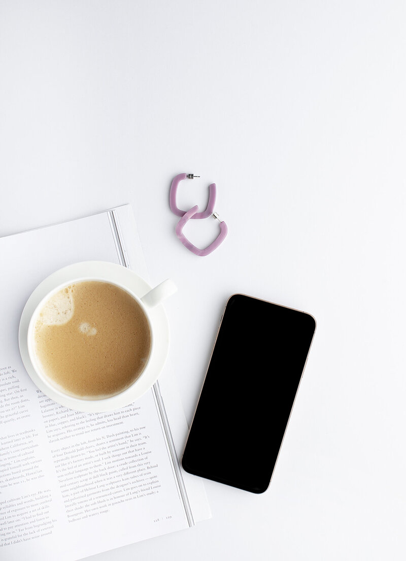 Flatlay of coffee mug with coffee next to an iphone and pink earrings