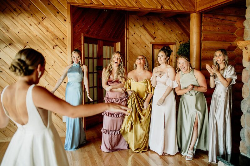 Bridesmaids wearing mismatched colorful dresses get a glance at the bride for the first time photographed by Emmie Verdell.