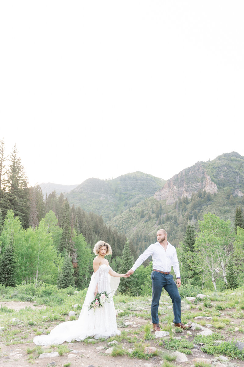 Bride & Groom holding hands walking through the mountains.