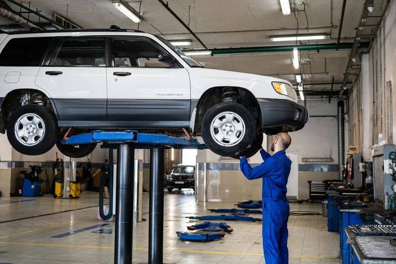 A mechanic in a blue uniform under a white car. and text with a 5 star review for Genuine Auto sns