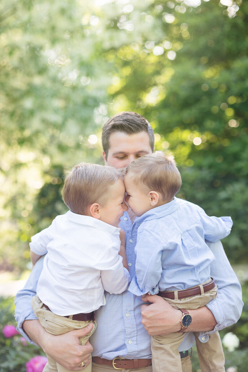 Dad holding his two sons in a green garden in louisville during their family photography session