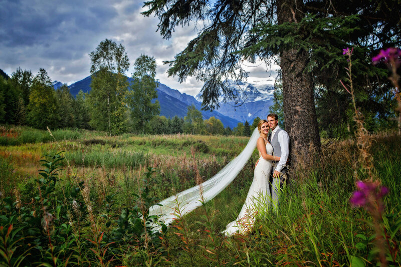 bride and groom lean on tree with mountains behind