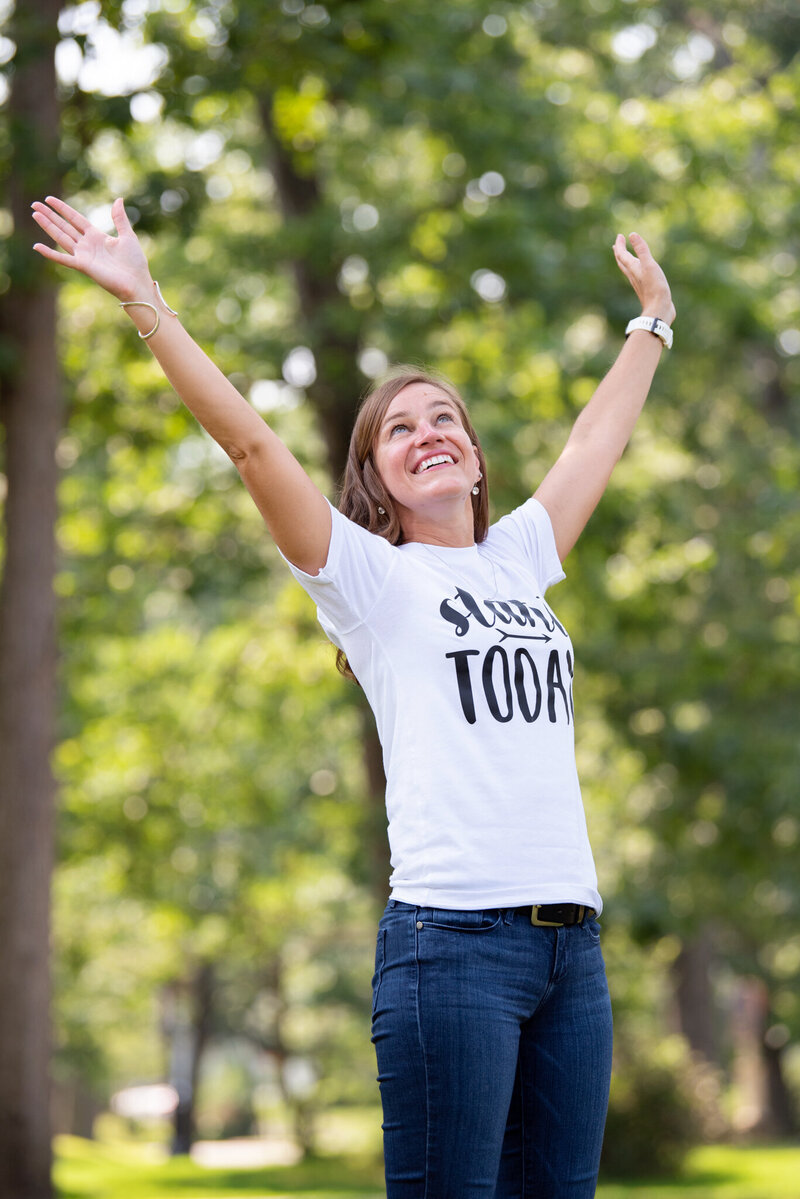 A woman sitting on a wooden bench at a park and holding her Canon DSLR camera.