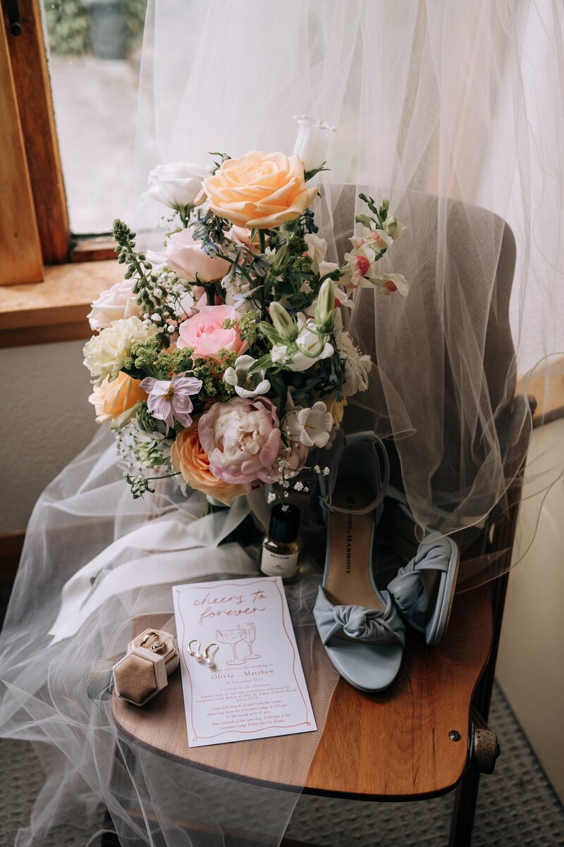 colourful pastel wedding  bouquet with pale blue shoes on chair with ivory veil