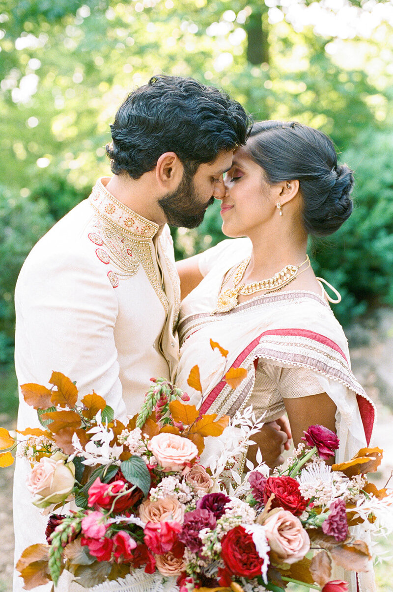 Traditional Indian Bride and Groom wedding with fall bridal bouquet in burgundy, maroon, red, copper, pink, dusty pink, and purple colors. Roses and fall branches highlight the fall florals. Design by Rosemary and Finch in Nashville, TN.