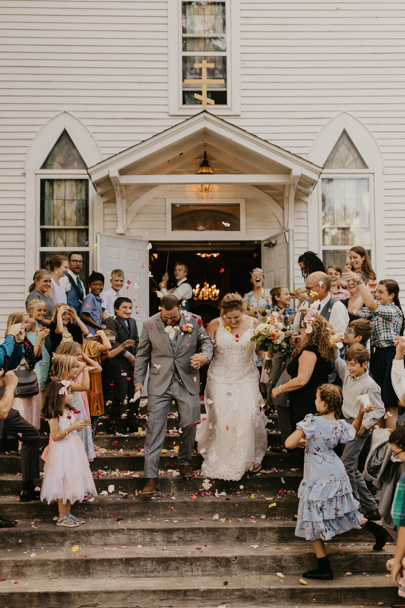 Couple walking out of the church after their ceremony with family lining the doorway and throwing flowers over them.