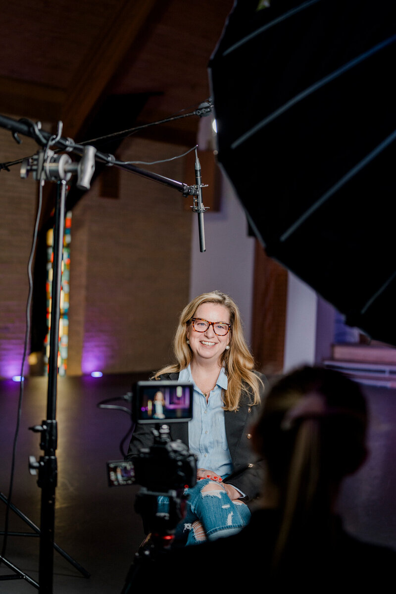 a woman smiles as she is interview under lights and on camera with a storyteller studios producer