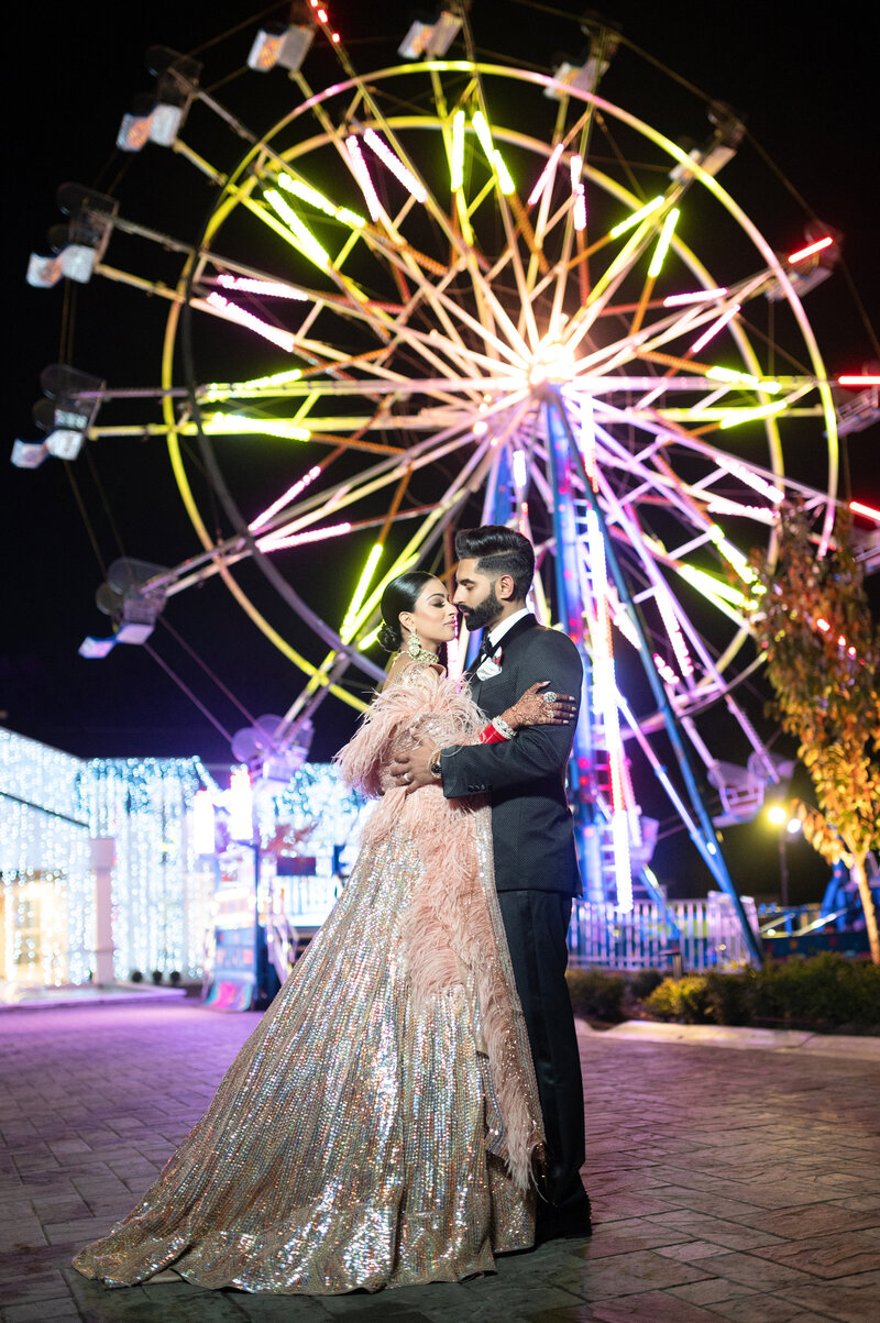 south asian bride and groom embracing each other in front of a lit farris wheel