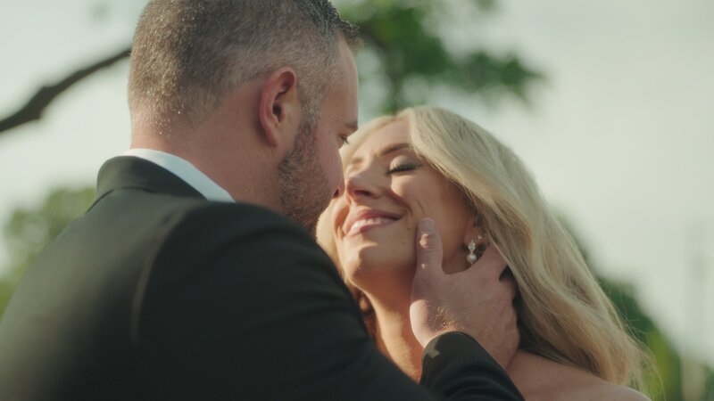 The groom leaned in to kiss the bride on the green lawn, surrounded by bridesmaids and groomsmen.