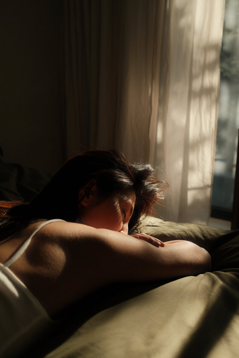 Woman resting peacefully in soft morning light, symbolizing intentional rest, nervous system regulation, and slow living as part of holistic self-care.

